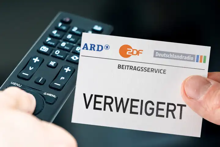 Germany - March 11, 2024: GEZ fees refused Symbolic image. Hand with ARD, ZDF and Deutschlandradio logo and the inscription: Refused in front of a remote control and a television. PHOTOMONTAGE
