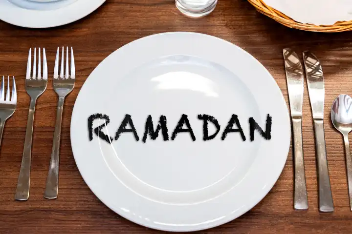 Ramadan, Schriftzug auf einem leeren Teller an einem gedeckten Tisch. FOTOMONTAGE