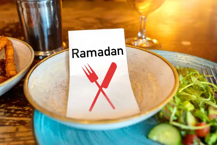 Ramadan, Schriftzug auf einer Serviette die auf einem Teller mit Nahrung liegt. FOTOMONTAGE