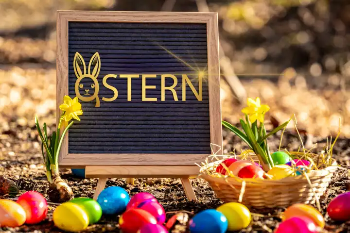 14 March 2024: Easter, golden lettering with an Easter bunny face on a panel surrounded by daffodils and colorful Easter eggs. PHOTOMONTAGE