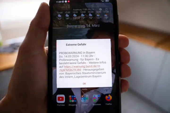 Mann hält Smartphone in der Hand mit Meldung über die Probewarnung in Bayern am 14 März um 11 Uhr. Extreme Gefahr Gefahrenwarnung auf dem Bildschirm