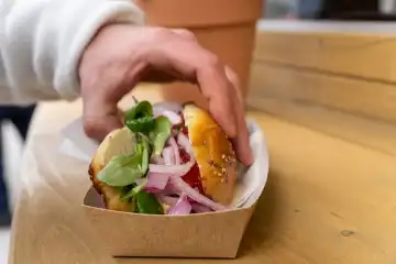 Hand hält vegetarisches Brötchen an einem Imbiss mit Blattsalat und Zwiebeln belegt