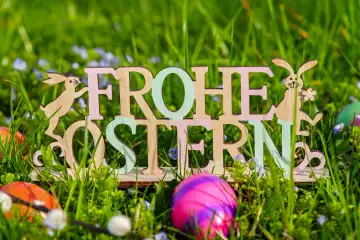 Frohe Ostern, Schriftzug aus Holz in einer grünen Wiese mit bunten Eiern