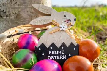 Osterhase in Osternest mit bunten Eiern mit dem Gruß: Frohe Ostern