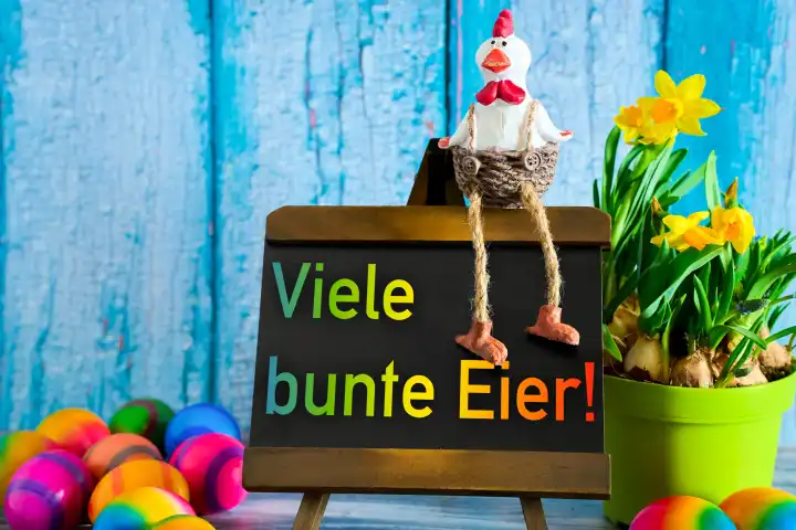 Augsburg, Bavaria, Germany - 23 March 2024: Many colorful eggs, inscription on a board next to colorful Easter eggs and daffodil flowers. A rooster sits on the board. PHOTOMONTAGE