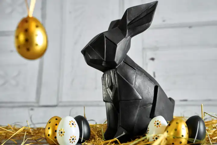 Abstrakte schwarze Osterhasen Figur mit goldenen Eiern in Stroh. Symbolbild Ostern Luxus und Elegant