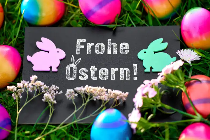  Augsburg, Bavaria, Germany - March 25, 2024: Greetings for Easter, Happy Easter! Lettering on a board in a green meadow with Easter bunnies and colorful Easter eggs. PHOTOMONTAGE