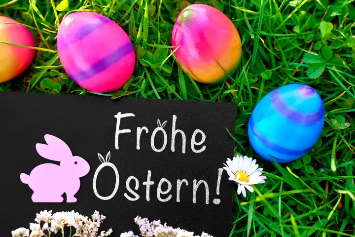 Augsburg, Bavaria, Germany - March 25, 2024: Greetings for Easter, Happy Easter! Lettering on a blackboard in a green meadow with an Easter bunny and colorful Easter eggs. PHOTOMONTAGE