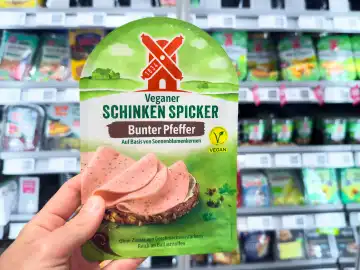Bavaria, Germany - March 27, 2024: Hand holding vegan Schickenspicker from the company Rügenwalder Mühle in front of a refrigerated shelf with vegan and vegetarian products in the supermarket