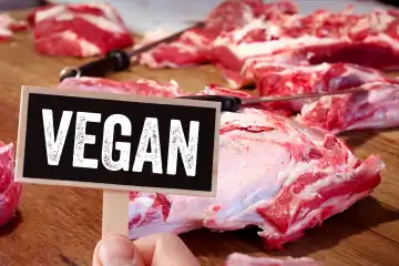 Veganes Fleisch - Fleischalternativen. Rohes Fleisch auf einer Arbeitsplatte mit Messer in einem Schlachthaus. Ein Schild mit der Aufschrift: Vegan für Alternativen zur veganen Ernährung. Fotomontage