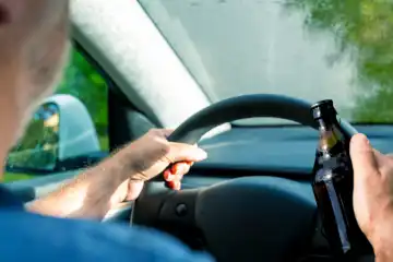 Person fährt Auto unter Konsum von Alkohol. Symbolbild betrunken Autofahren, Promillegrenze und Alkohol am Steuer. FOTOMONTAGE