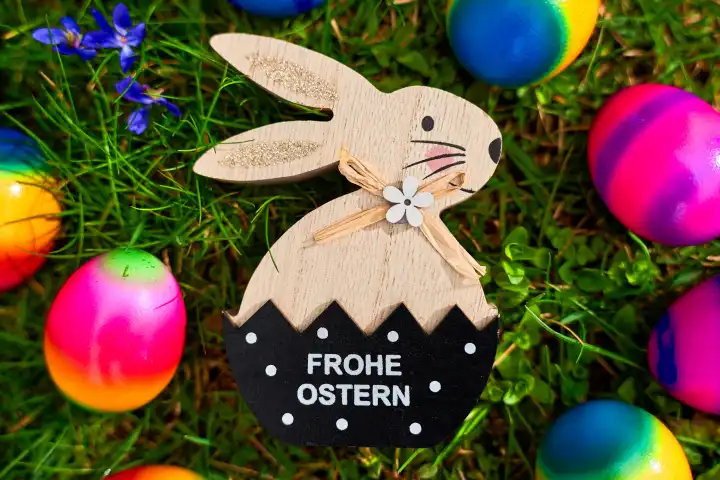 Augsburg, Bavaria, Germany - 28 March 2024: Wooden Easter bunny in a green meadow with colorful eggs and the lettering: Happy Easter