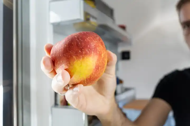 Ein Mann holt einen roten Apfel aus einem Kühlschrank
