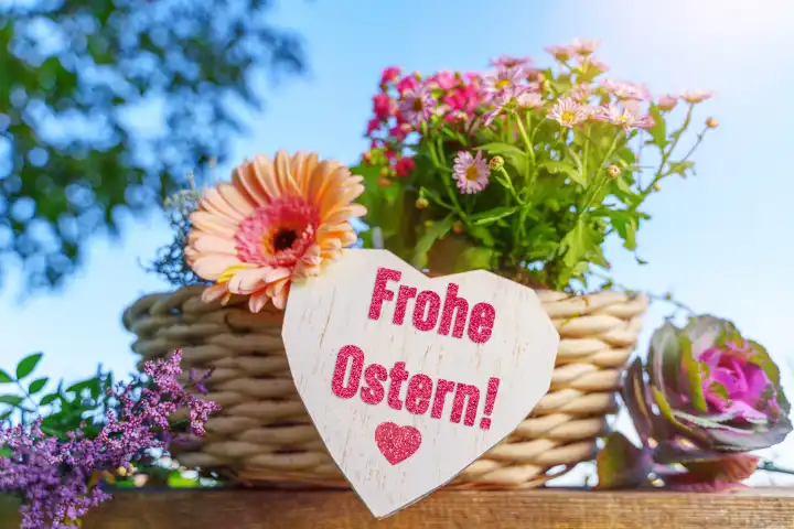 Frohe Ostern! Schriftzug auf einem Herz an einem bunten Blumengesteck im Frühling. FOTOMONTAGE