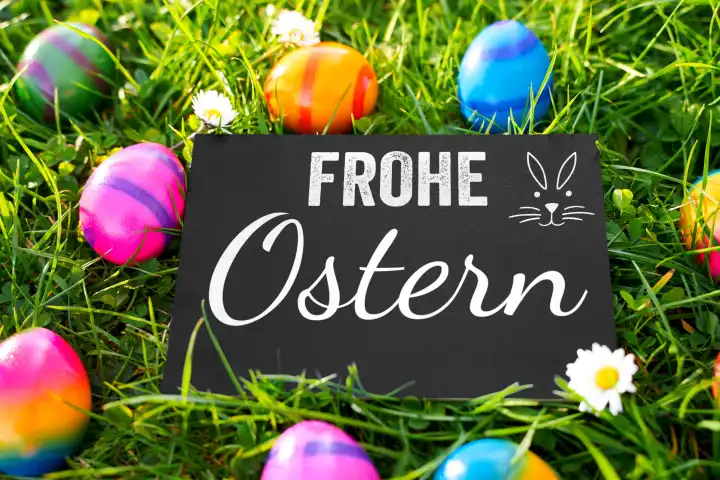 Frohe Ostern! Grüße auf einer Tafel in einer grünen Wiese mit gefärbten Ostereiern. Gruß zu Ostern. FOTOMONTAGE