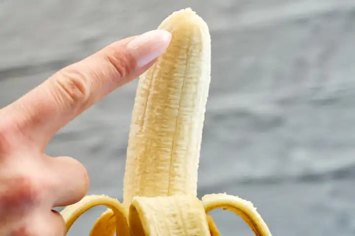 Eine Frau berührt mit der Hand eine geschälte Banane