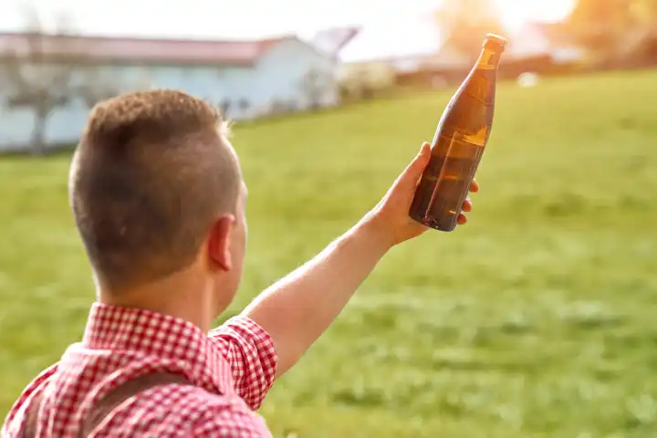 Bayer in Lederhose und Tracht hält eine Flasche Bier. Feierabendbier Konzept