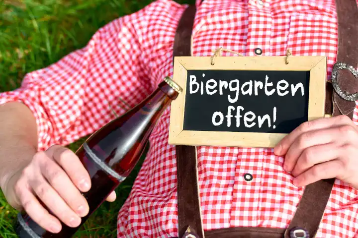 April 9, 2024: A man in lederhosen holds a sign with the inscription: Beer garden open. PHOTOMONTAGE