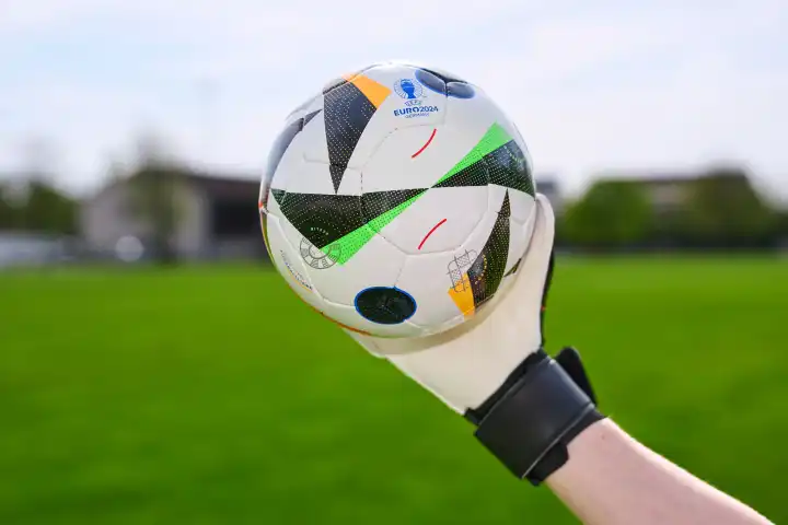 Themenbild: EURO 2024 offizieller Fußball Spielball von Sportausrüster Adidas. Hand hält Ball auf einem Fußballfeld. Fußball-Europameisterschaft 2024
