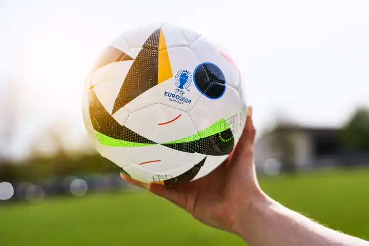 Themenbild: EURO 2024 offizieller Fußball Spielball von Sportausrüster Adidas. Hand hält Ball auf einem Fußballfeld. Fußball-Europameisterschaft 2024