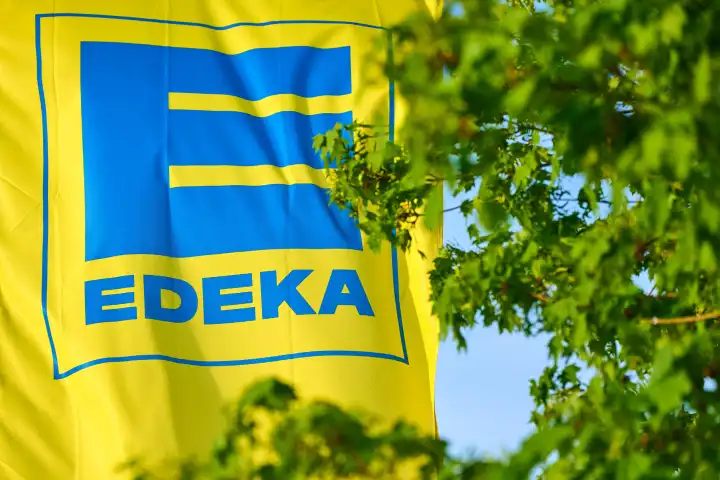Fahne vom deutchen Supermarkt und Lebensmittelhändler EDEKA vor grünen Bäumen
