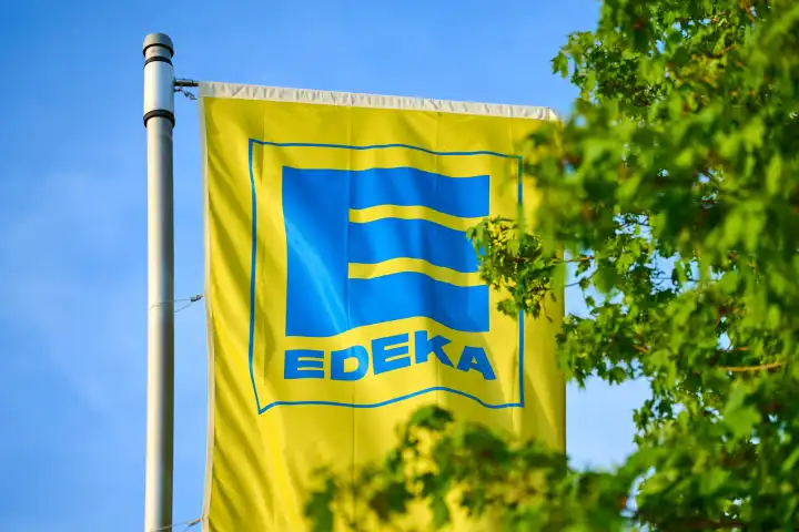 Fahne vom deutchen Supermarkt und Lebensmittelhändler EDEKA vor grünen Bäumen