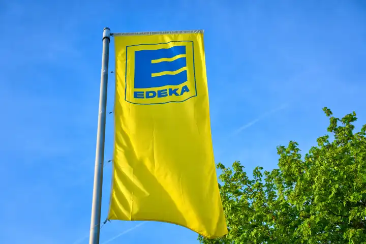 Augsburg, Bavaria, Germany - April 13, 2024: Flag of the German supermarket and food retailer EDEKA in front of green trees