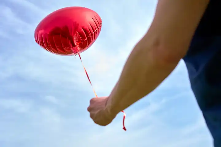 Junger Mann hält einen roten Helium Luftballon in Herzform. Symbolbild Liebe und Romantik