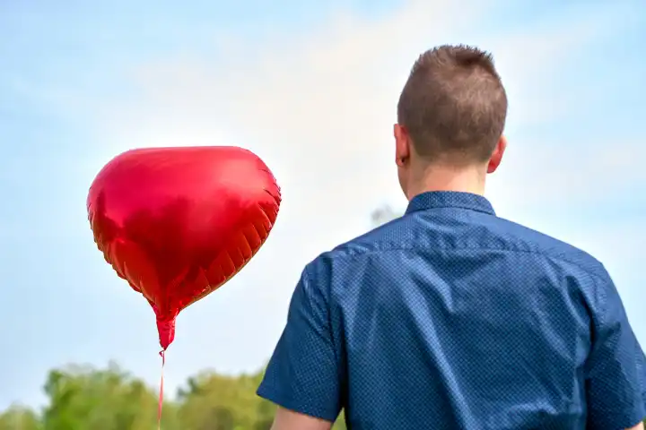 14 April 2024: Young man holding a red helium balloon in the shape of a heart. Symbolic image of love and romance