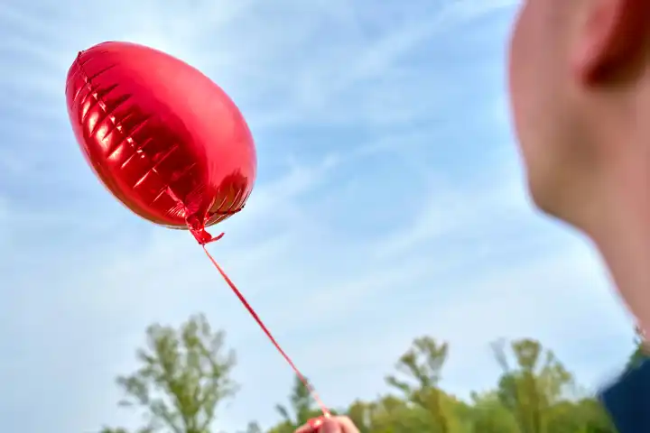 Junger Mann hält einen roten Helium Luftballon in Herzform. Symbolbild Liebe und Romantik