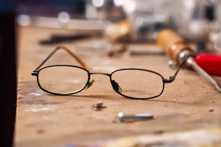 Kaputte alte Brille auf einer Werkbank in einer Werkstatt. Symbolfoto Arbeitsunfall und Insolvenz