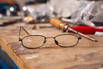 Kaputte alte Brille auf einer Werkbank in einer Werkstatt. Symbolfoto Arbeitsunfall und Insolvenz
