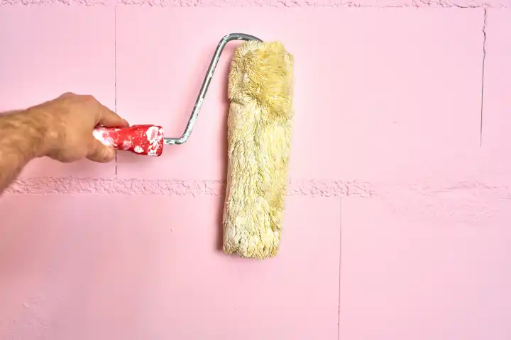 Augsburg, Bavaria, Germany - 13 April 2024: Symbolic image Painting a colorful wall with a paint roller. Hand holding a paint roller