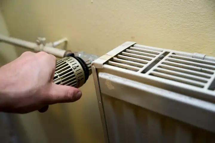 Die Hand von einem Mann dreht am Thermostat von einem Heizkörper. Heizung