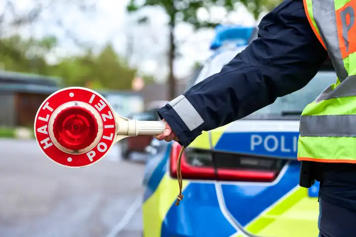 Symbolbild Polizeikontrolle, Polizei vor Polizeiauto mit Polizeikelle an einer Straße