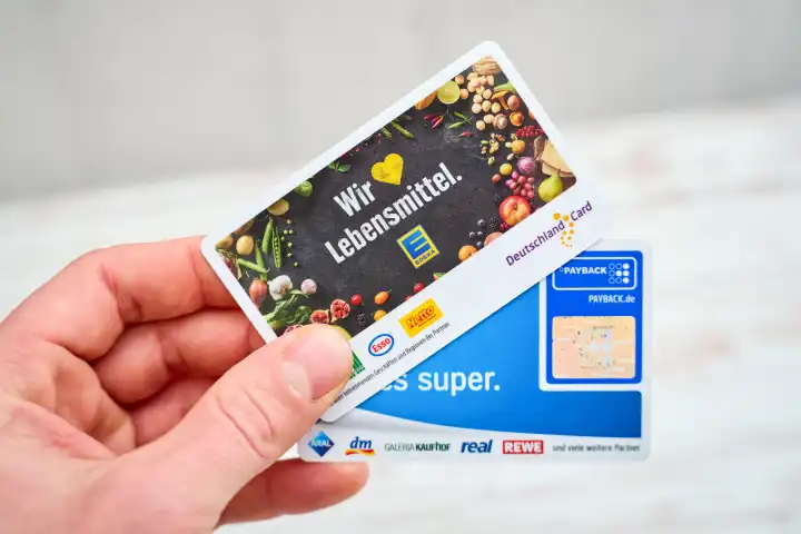 Hand hält zwei Bonusprogramm Kundenkarten von Payback und die Deutschland Card