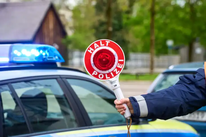Polizist hält eine Polizeikelle mit Aufschrift Halt Polizei vor ein Polizeiauto mit Blaulicht