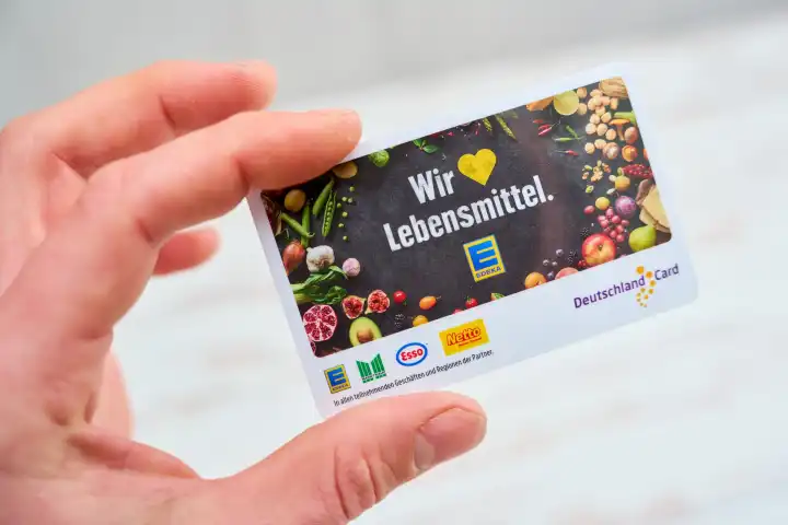 Augsburg, Bavaria, Germany - April 17, 2024: A customer's hand holds a Deutschland Card. Bonus program customer card from Edeka, Netto, Esso and Marktkauf