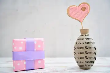 Verpacktes Geschenk neben einer Deko Vase mit Schriftzug: Schönen Muttertag! FOTOMONTAGE