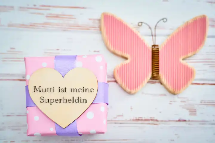 Augsburg, Bavaria, Germany - April 17, 2024: Mom is my superhero! Mother's Day saying on a wooden heart on a gift. PHOTOMONTAGE