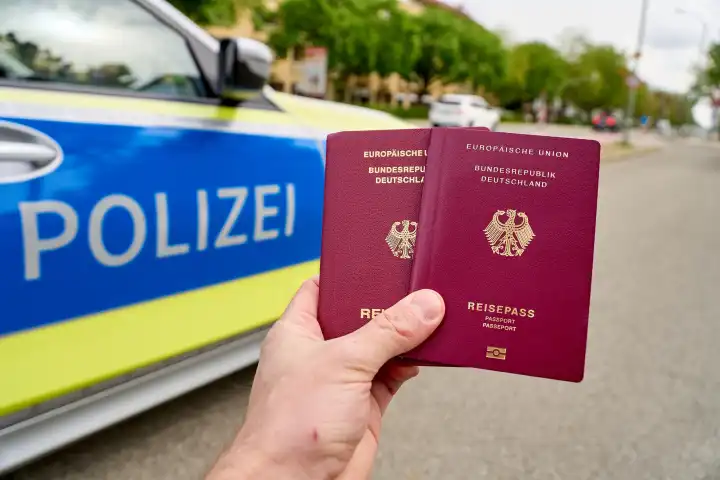 Augsburg, Bavaria, Germany - April 19, 2024: Hand holds passport of the Federal Republic of Germany in front of a police car. Symbol photo border control