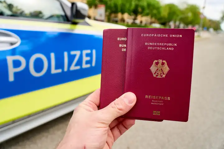 Augsburg, Bavaria, Germany - April 19, 2024: Hand holds passport of the Federal Republic of Germany in front of a police car. Symbol photo border control