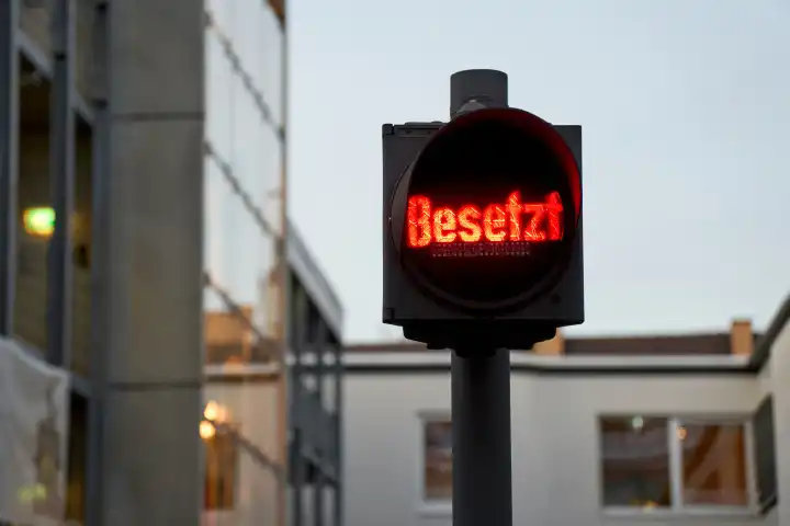 Augsburg, Bavaria, Germany - December 3, 2023: Red traffic light with the lettering: Occupied, in front of a parking garage