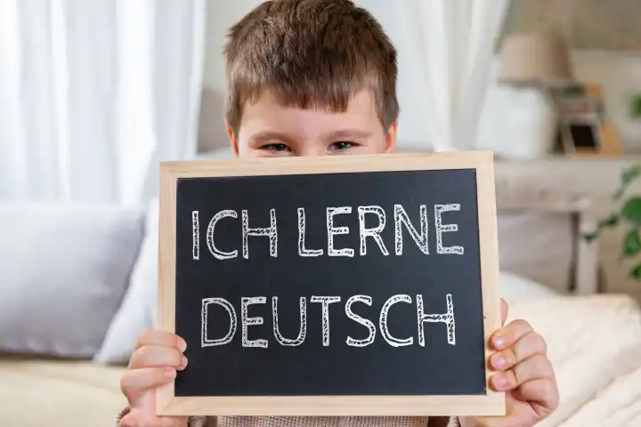 Kind hält eine Tafel mit der Aufschrift: Ich lerne Deutsch. Sprachunterricht und Migration Konzept. FOTOMONTAGE
