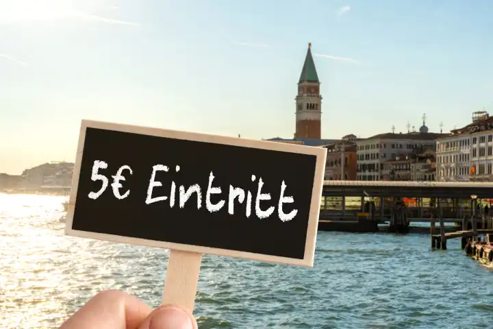 23 April 2024: Symbolic photo Venice charges admission for day tourists. A hand holds a board with the inscription: 5€ entrance fee, in front of the Italian city of Venice. PHOTOMONTAGE