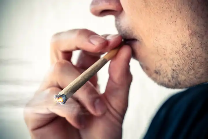 Mann raucht bzw. kifft einen Joint aus Cannabis bzw. THC in der Öffentlichkeit. Nahaufnahme beim Kiffen nach der Cannabis-Legalisierung. FOTOMONTAGE