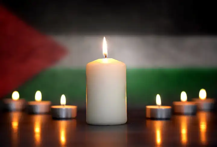 April 24, 2024: Burning candles in front of a Palestine flag. Symbolic photo of mourning for the fallen soldiers and civilians in the Middle East war and conflict. PHOTOMONTAGE