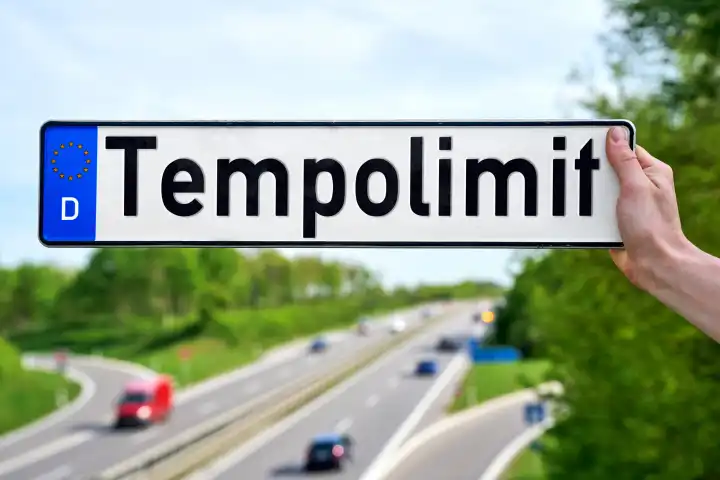 Hand hält vor eine Autobahn ein Kfz-Kennzeichen mit Aufschrift: Tempolimit. FOTOMONTAGE