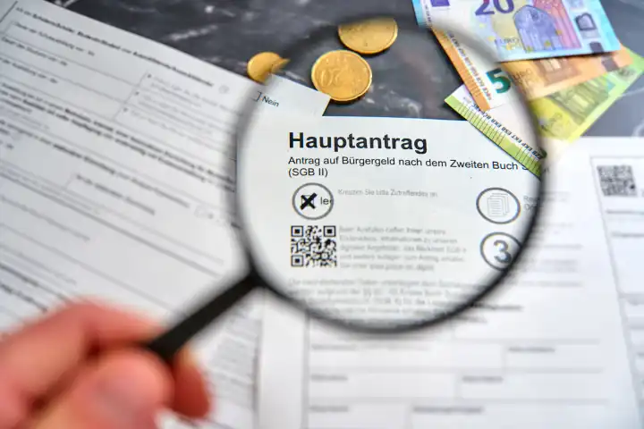 Augsburg, Bavaria, Germany - April 25, 2024: Hand holding magnifying glass over the word Bürgergeld on the main application for Bürgergeld from the Agentur für Arbeit