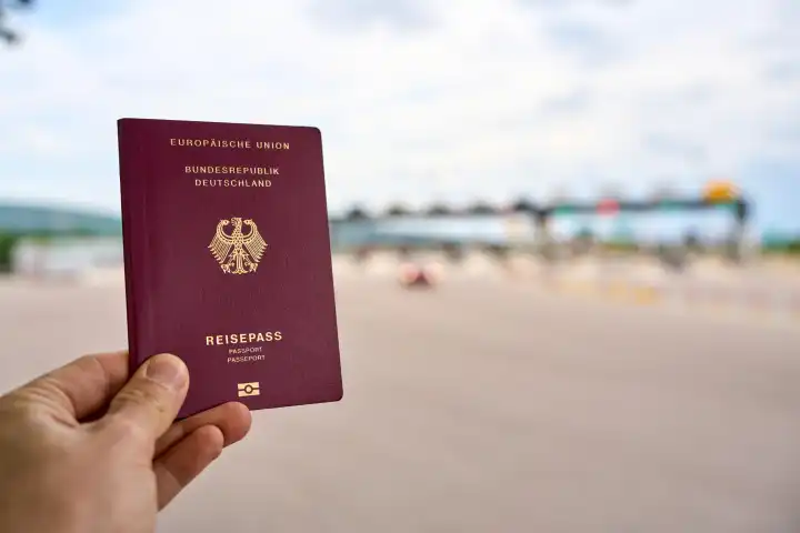 Hand hält einen Reisepass der Bundesrepublik Deutschland vor einen Grenzübergang. Migration und Einwanderung Konzept